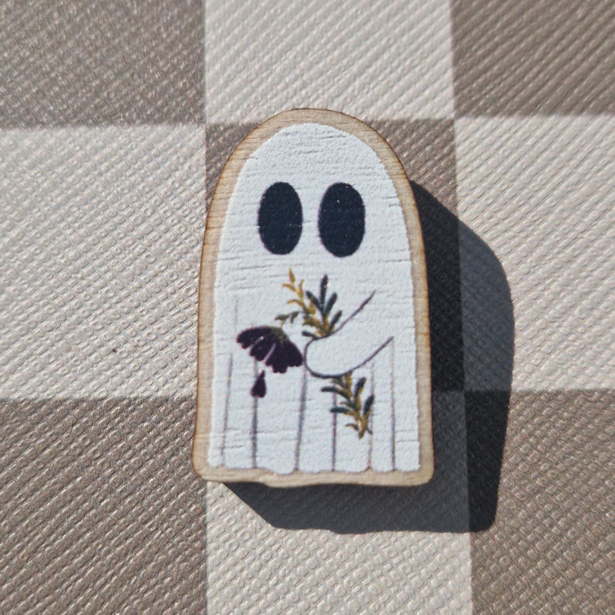 A small wooden magnet charm designed as a ghost with flowers, displayed on a checkered background.