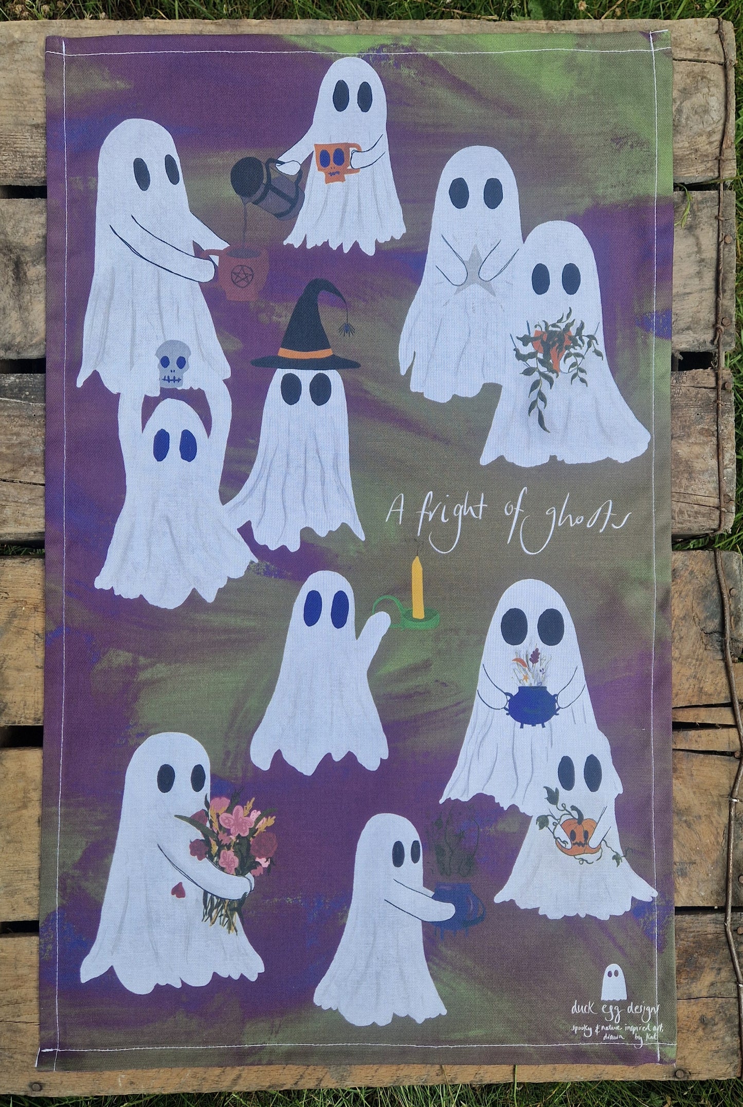 Decorative tea towel with ghost illustrations on a wooden surface