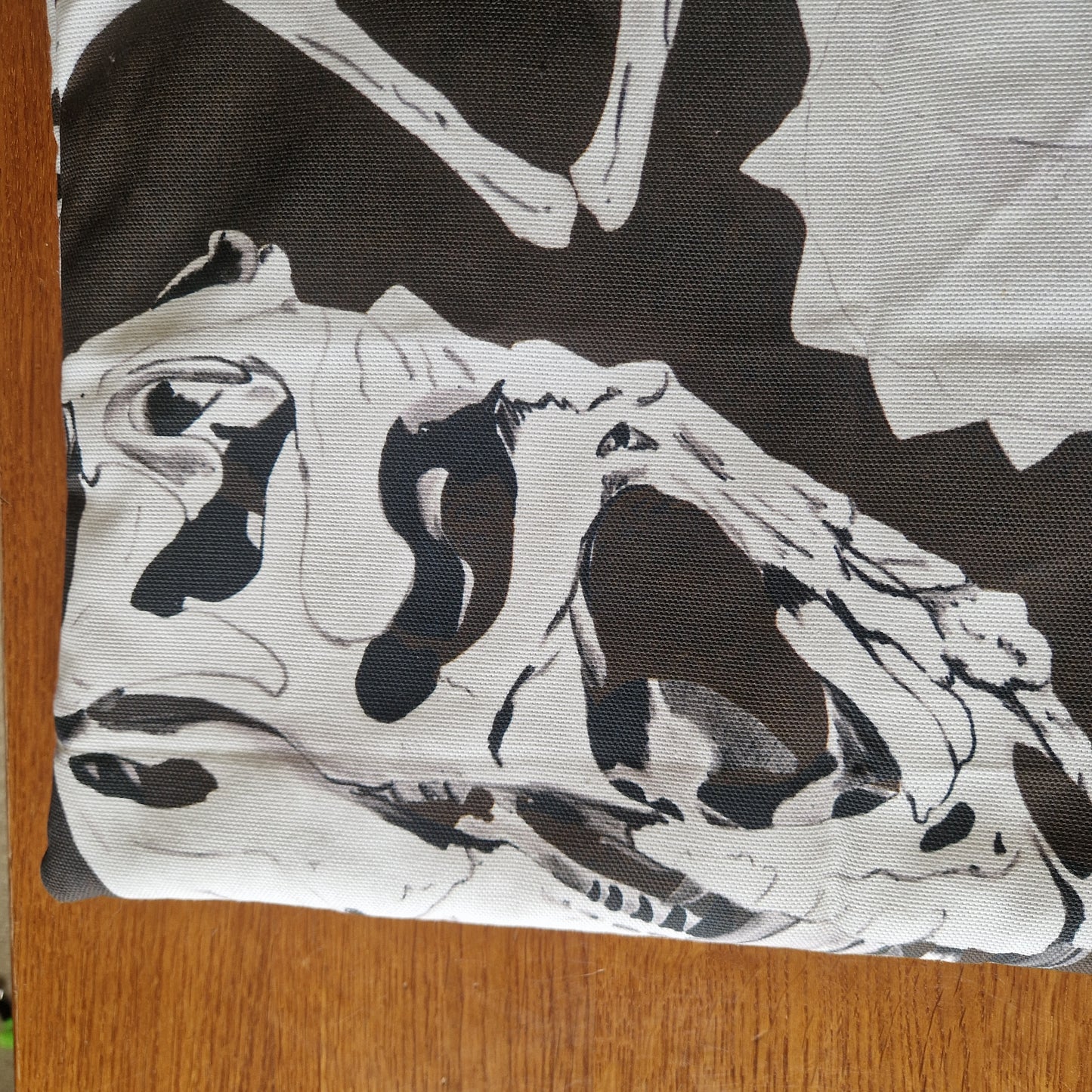 The Dinosaur Bones Small Laptop/Tablet Sleeve by Duck Egg Designs is a handmade pouch crafted from recycled fabric, featuring a black and white dinosaur skull illustration, shown close-up on a wooden surface.