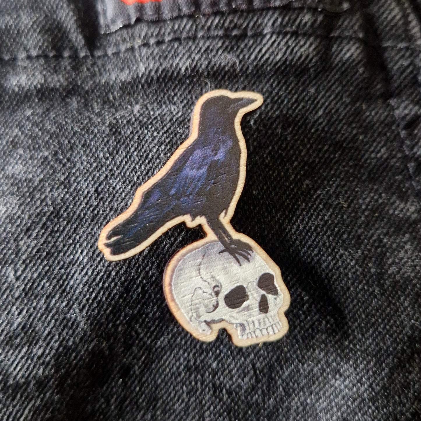 Pin with a crow on a skull design on denim dungarees.