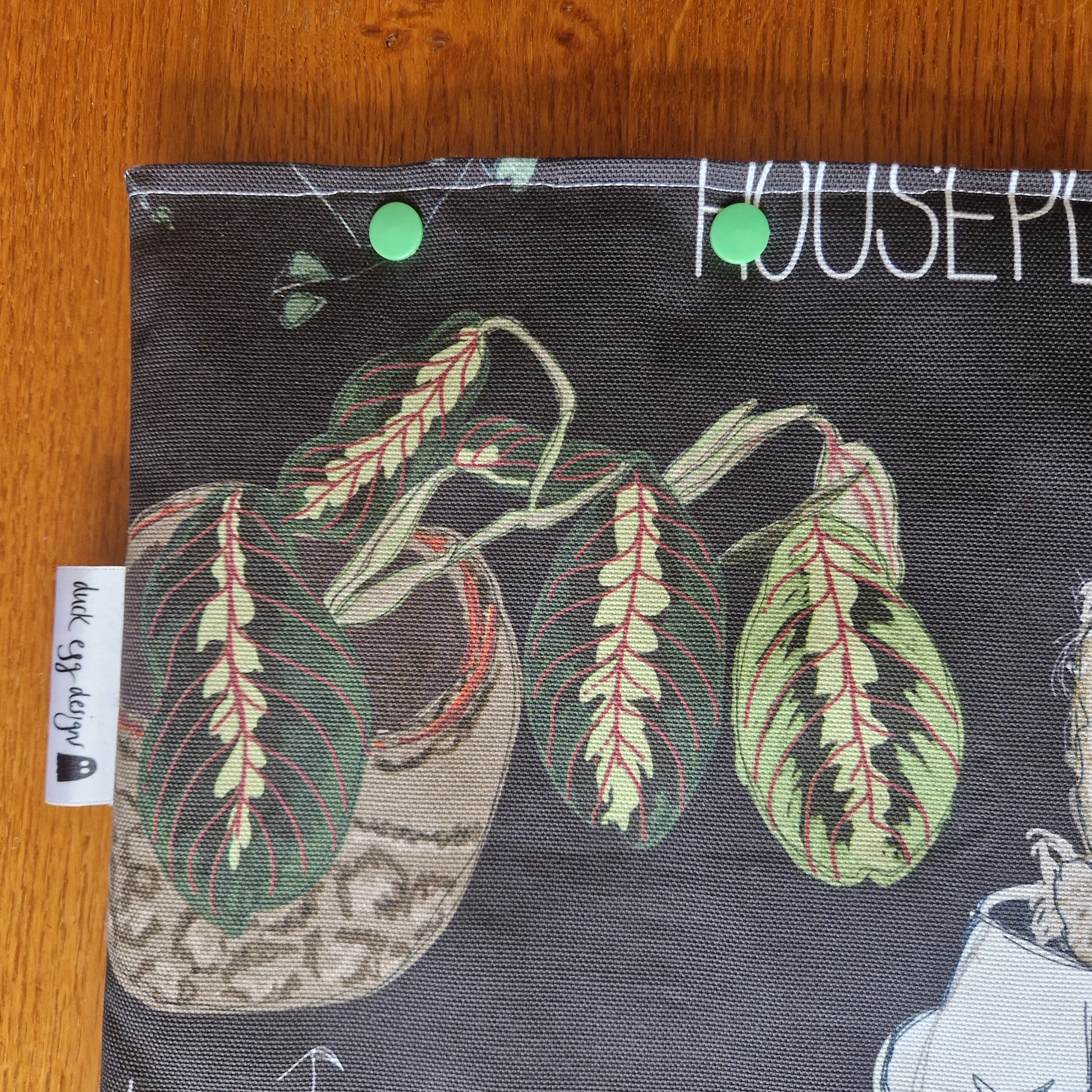 The Common Houseplants Small Laptop/Tablet Sleeve by Duck Egg Designs features a handmade illustration of a potted prayer plant with green leaves and red veins, crafted from recycled fabric. A white label reads Duck Egg Designs.