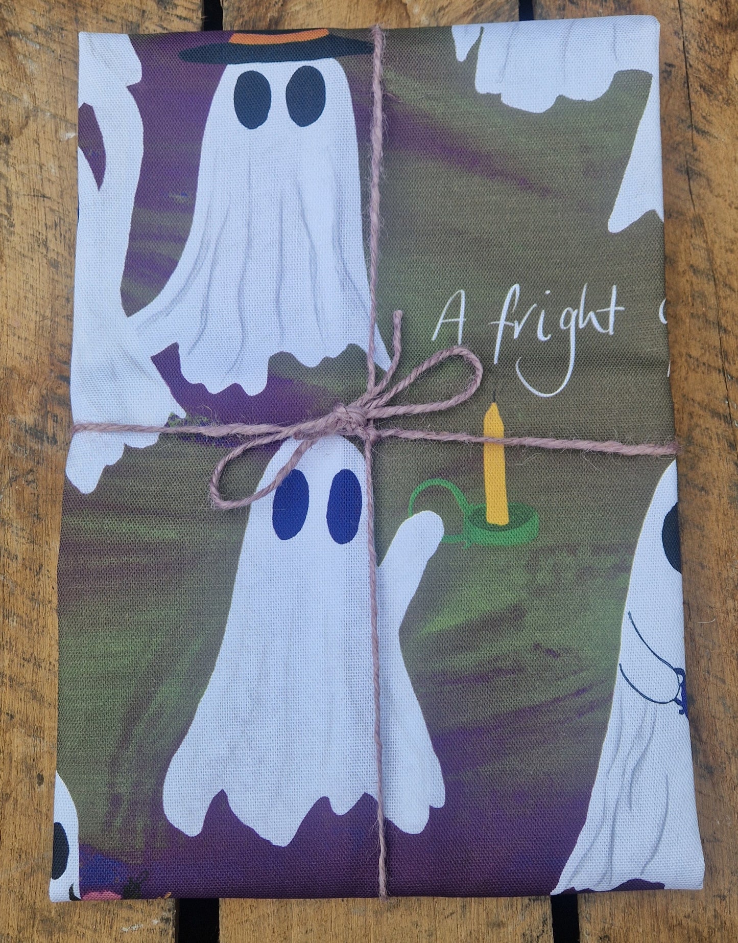 Halloween themed tea towel with a green and purple fabric colour on a wooden background.