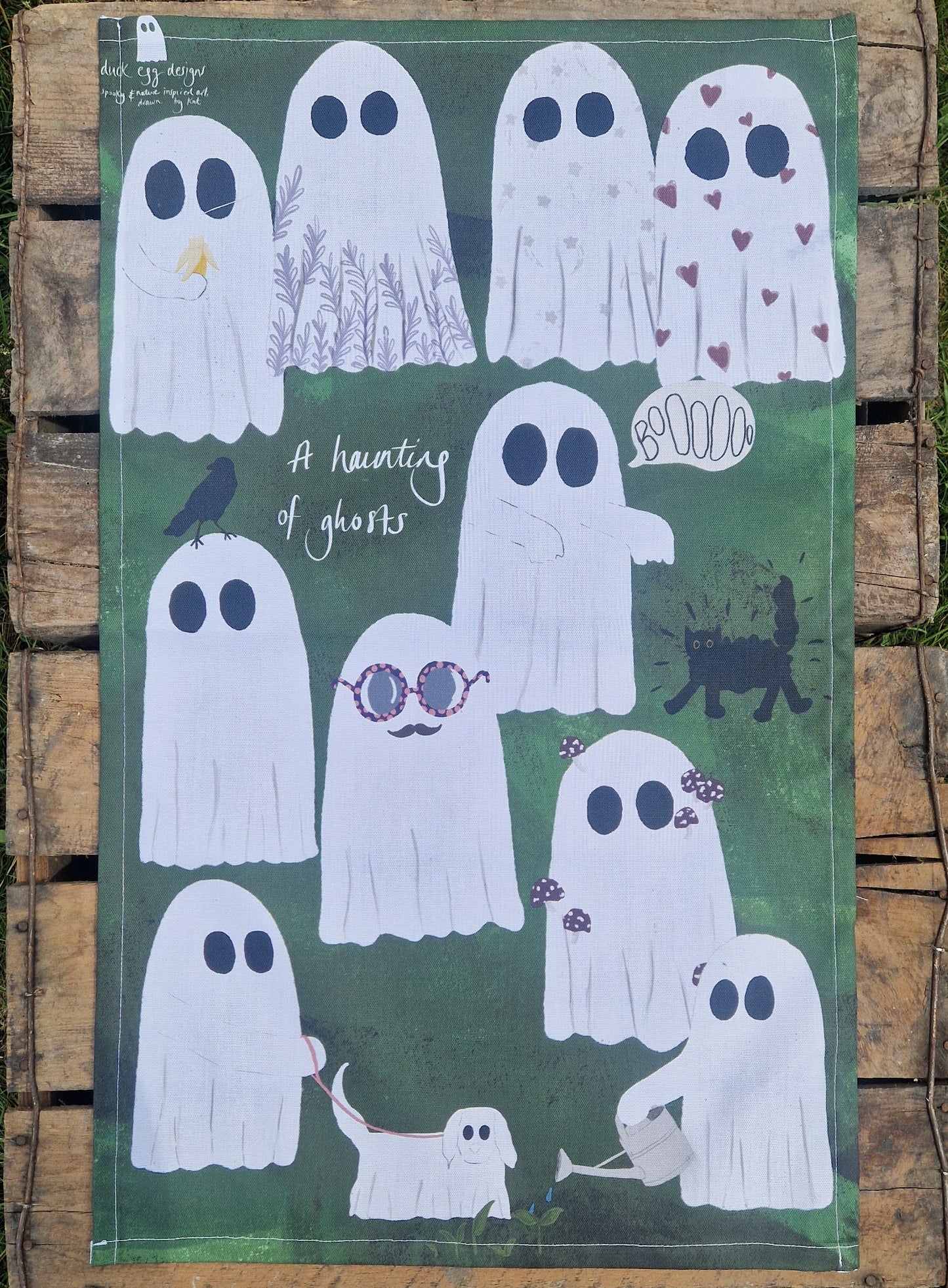 Ghost tea towel with a green background sits on wooden boards.