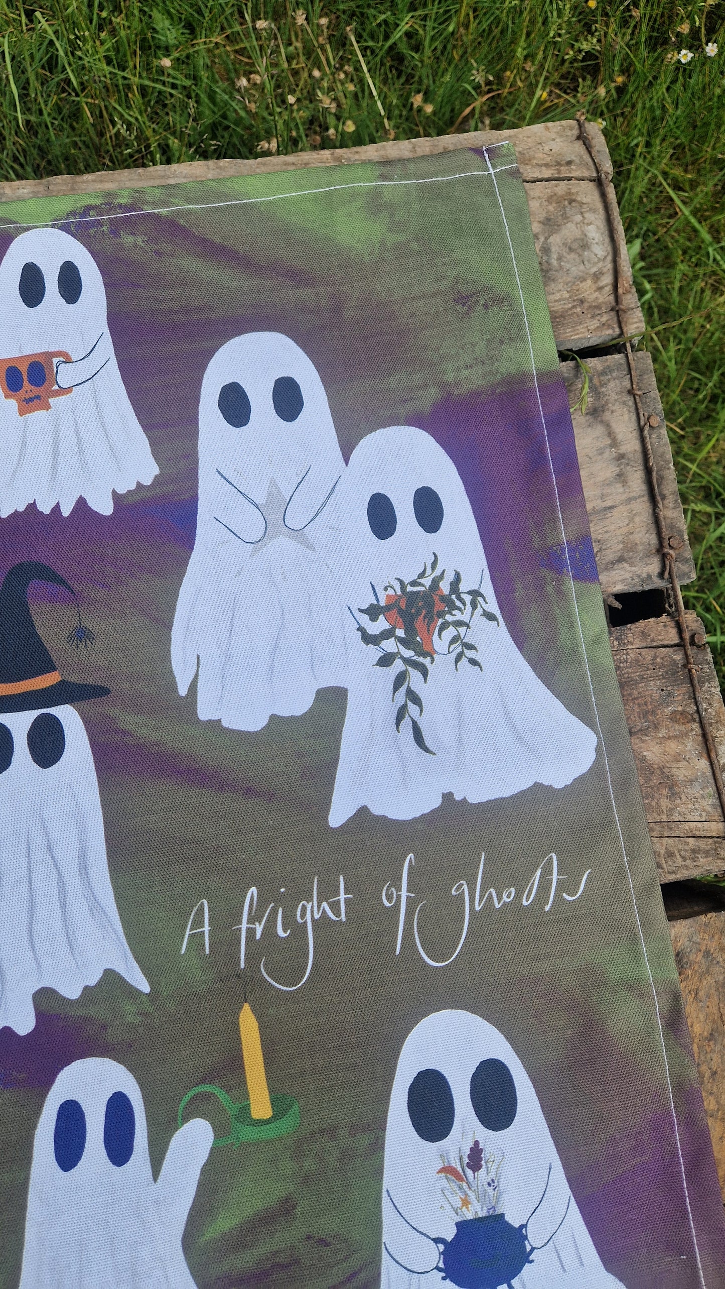 Decorative tea towels with ghost illustrations and text on a wooden surface outdoors.