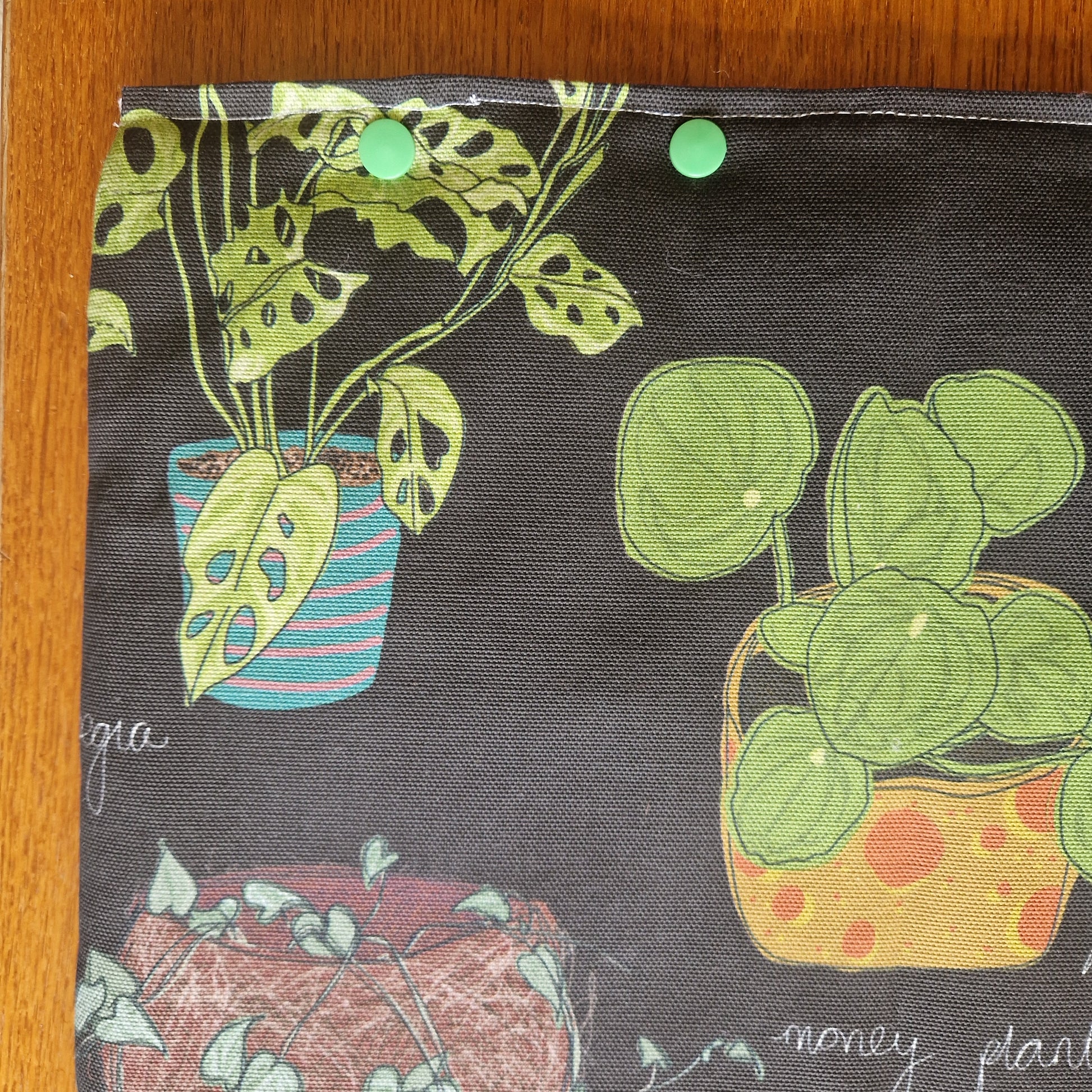 The Common Houseplants Small Laptop/Tablet Sleeve by Duck Egg Designs features handmade, recycled fabric with vibrant illustrations of potted plants and green snaps, providing secure and stylish protection for your device.