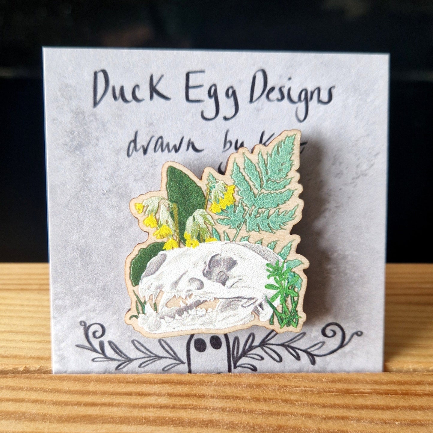 Pin with skull and leaves design on a card labeled 'Duck Egg Designs'.