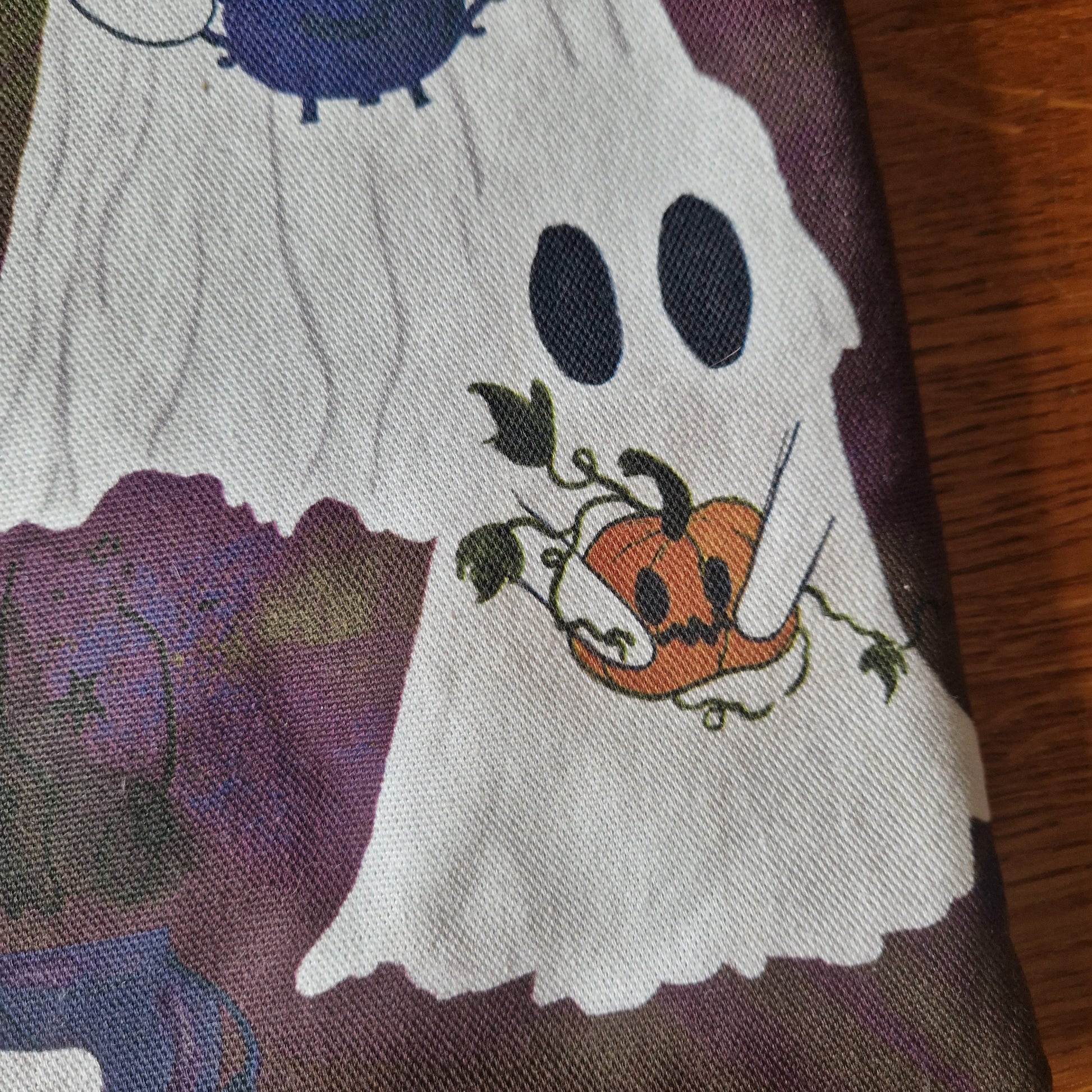 The A Fright Of Ghosts Book Sleeve by Duck Egg Designs is a reusable cover made from upcycled fabric, featuring a white ghost with black eyes holding a jack-o-lantern on a dark purple Halloween-themed background.