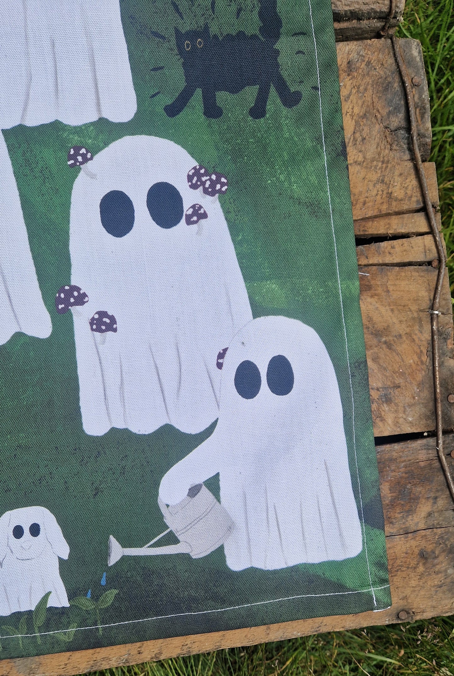 Ghost tea towel with a green background sits on wooden boards.