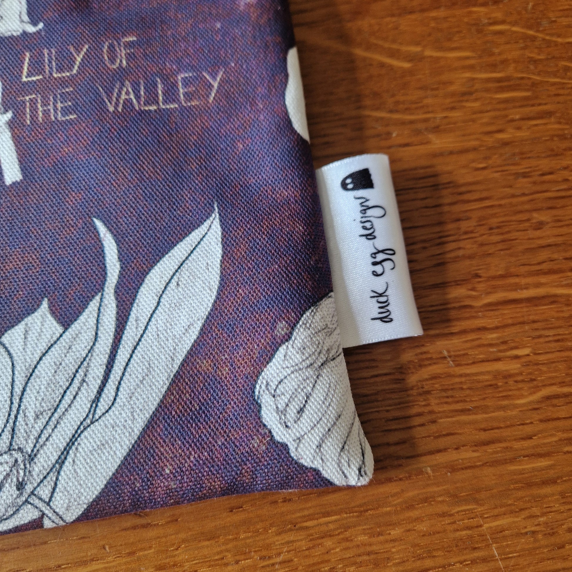 A close-up of the Poison Plants Kindle Pouch by Duck Egg Designs shows a floral print and a logo tag—perfect as a unique handmade Kindle sleeve or case.