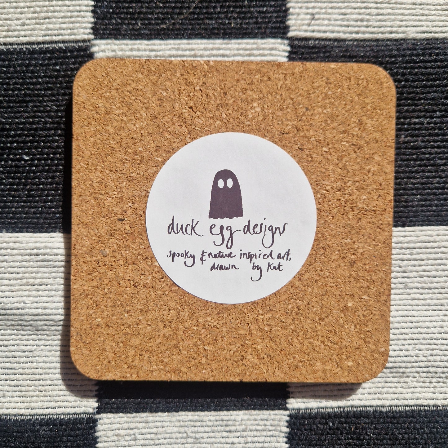 The British Fungi Coaster by Duck Egg Designs is UK-printed with a cork base, featuring a round white label and a fungi illustration. The coaster is shown resting on a black and white striped cloth.
