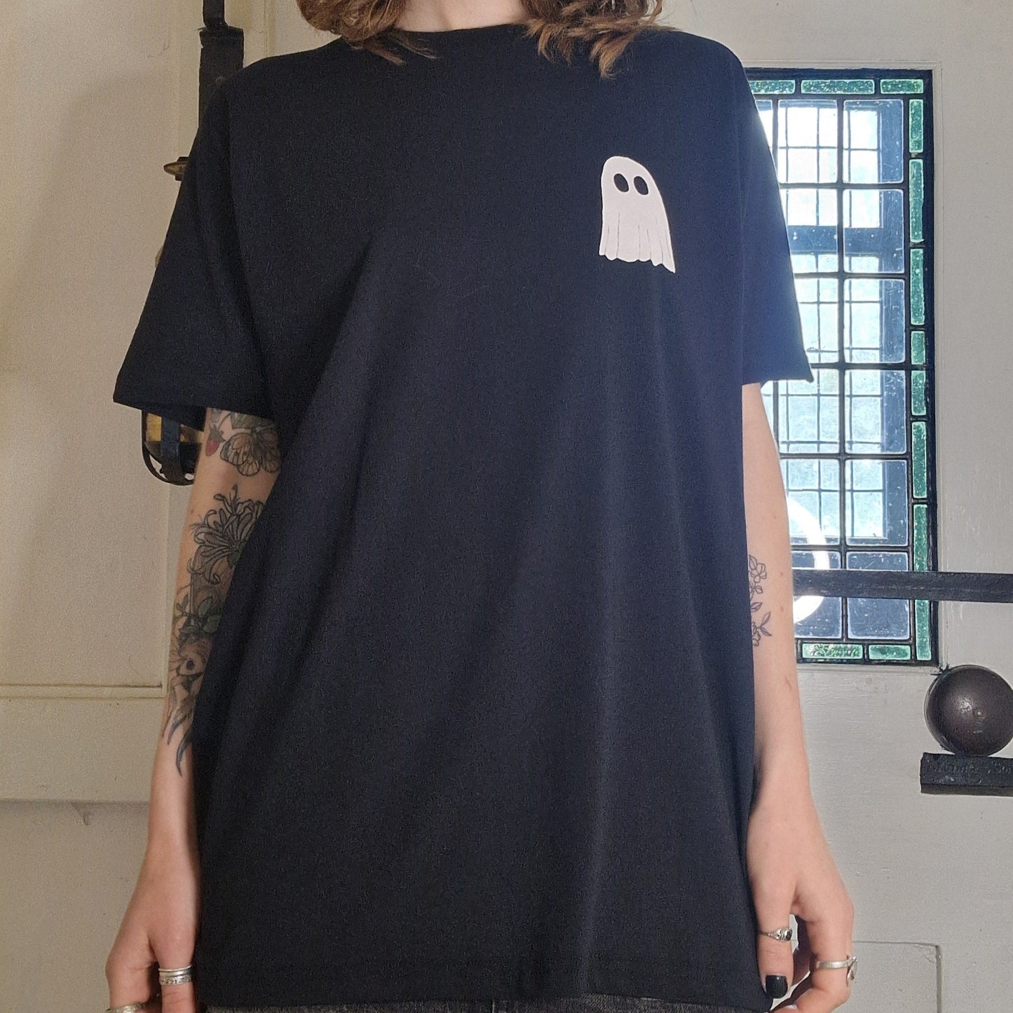 Person wearing a black t-shirt with a white ghost design in an indoor setting.