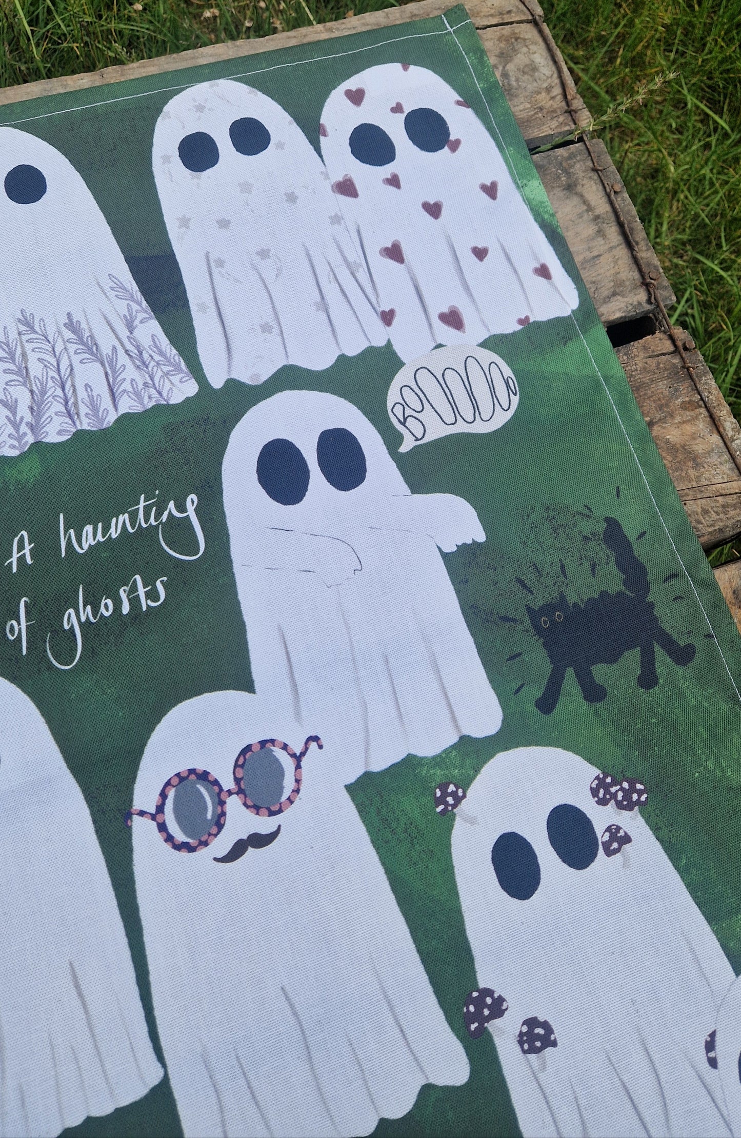 Ghost tea towel with a green background sits on wooden boards.