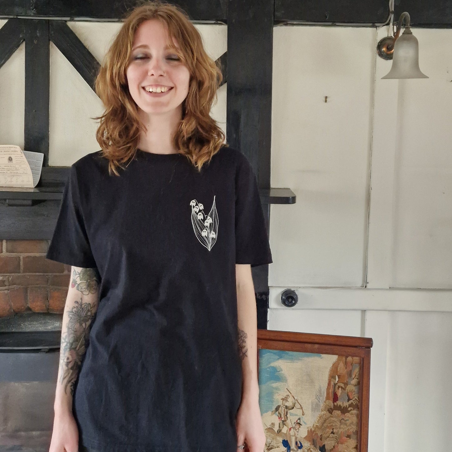 Person wearing a black t-shirt with a graphic design in a room with wooden panelling and a fireplace.