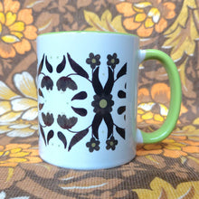 Load image into Gallery viewer, A white mug with a green handle and inside sits in front of a brown and white floral background. The mug features a symmetrical 70s inspired floral pattern in brown and green.
