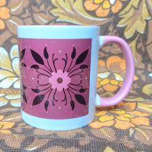 Load image into Gallery viewer, A white mug with a pink handle sits on a brown, white and yellow floral background. The mug features a deep pink rectangle with a brown, pink and yellow symmetrical floral pattern.
