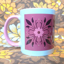 Load image into Gallery viewer, A white mug with pink handle sits on a brown white and yellow floral background. The mug features a pink and brown floral symmetrical pattern on a deep pink background. You can see it’s pink handle on the left.
