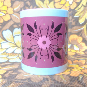 A white and pink mug featuring a symmetrical floral pattern sits on a floral fabric background.