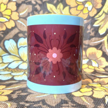 Load image into Gallery viewer, A white mug with a yellow handle and inside sits in front of a brown and yellow floral background. The mug features a brown rectangle across it with a dark orange and black floral pattern.
