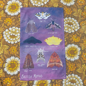 A purple teatowel featuring eight different British moths, sits on a white, yellow and brown floral background.