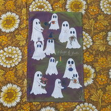 Load image into Gallery viewer, A green and purple tea towel featuring ‘A fright of ghosts’ sits on a brown, white and yellow floral background. They are a range of ghosts on the design from a couple sharing a coffee to ones holding pumpkins, a skull, a houseplant, a star, a bunch of others and even a candle.
