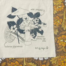 Load image into Gallery viewer, A closer view of the entire design on the bag, showing the fungi and wild strawberry design. To the right and below the bag you can see white, brown and yellow floral fabric.
