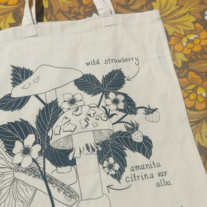 A close up of the natural tote so you can see the fungi and wild strawberry plant in more detail. To the right of the bag you can see yellow and brown floral patterned fabric.
