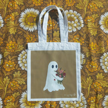 Load image into Gallery viewer, A white tote bag sits on a retro floral brown, white and yellow patterned background. The tote features a golden yellow rectangle with a ghost hugging a bunch of flowers. To the bottom right of the square is the Duck Egg Designs logo in white.
