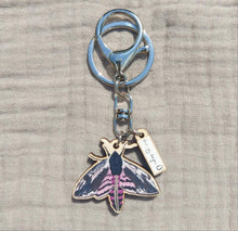 Load image into Gallery viewer, A photo of the full keyring which features a black and pink privet hawk moth and a small charm with the Duck Egg Design logo.
