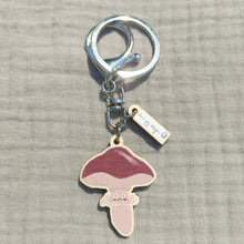 Load image into Gallery viewer, A light brown fungi keyring with a dark brown cap sits on a light grey fabric background. The keyring features a little worried face on the stalk, and above the mushroom charm you can see a mini charm with the Duck Egg Designs logo. The  keyring has both a split ring and a lobster clasp.
