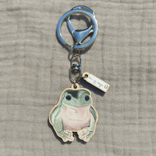 Load image into Gallery viewer, A green and pink frog keyring with a split ring and a lobster clasp sits on a light grey fabric background. Just above the frog you can see a second mini charm with the white and black Duck Egg Designs logo.
