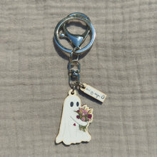 Load image into Gallery viewer, A ghost keyring with a split ring and a lobster clasp sits on a light grey background. The ghost is white with black eyes and hugs a bunch of richly coloured flowers in red, dusky pink and mustard yellow. 
