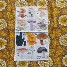 Load image into Gallery viewer, An off white tea towel featuring 12 different British fungi in rows of three with their names in black handwriting next to them. Behind the tea towel is a warm brown retro floral patterned fabric.
