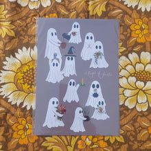 Load image into Gallery viewer, A dusky purple print featuring the words ‘A fright of ghosts’ in white handwriting on the right, surrounded by a group of ghosts doing different things. Behind the print you can see a warm brown retro floral patterned background.
