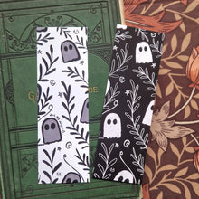 Load image into Gallery viewer, An image of the front and back of the bookmark together showing the black and white versions of the ghost and vine pattern. Behind the bookmarks you can see an old green gardening book behind which is a brown floral patterned fabric.
