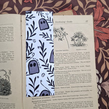 Load image into Gallery viewer, On an open vintage book for gardening sits on a brown retro vintage floral background with the white side of the bookmark on view featuring a pattern with leafy vines, ghosts, crescent moons and stars.

