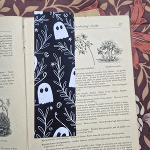 An open vintage gardening book sits on a brown floral patterned background. The book has a black bookmark featuring a white line pattern of ghosts among a leafy vine with stars and crescent moons. 