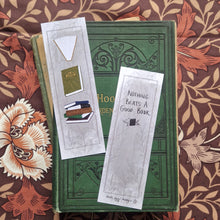 Load image into Gallery viewer, Two bookmarks sit in an open vintage gardening book showing the front and back of the bookmark. Behind the book you can see a brown retro floral fabric. The bookmark has a textured grey background with a dark grey border and leafy vines pattern. Running down the front of the bookmark are three different book illustrations while on the back there are words in black handwriting that say ‘Nothing beats a good book’ at the bottom of the bookmark is the duck egg designs logo.
