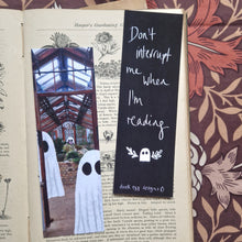 Load image into Gallery viewer, An old book sits open with a brown floral background visible to the right and top of it. The book has two bookmarks on it - one features a greenhouse with ghosts in it while the other is black and features the words ‘Don’t interrupt me when I’m reading’ in white above a ghost with little leafy vines around it. At the bottom of the bookmark you can see a white duck egg designs logo.
