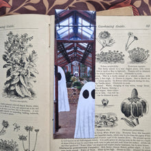 Load image into Gallery viewer, A vintage gardening book lies open with a bookmark in it. The bookmark has a greenhouse with ghost in it on the front and the book sits on a brown floral background.
