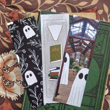 Load image into Gallery viewer, Three bookmarks sits on top of an old green book Ona brown retro floral background. The one on the left is black with a white leafy vine and ghost design  with stars and crescent moons. The middle bookmarks is a textured grey with books running down the centre. The bookmark on the right has a design with ghosts in a greenhouse. 
