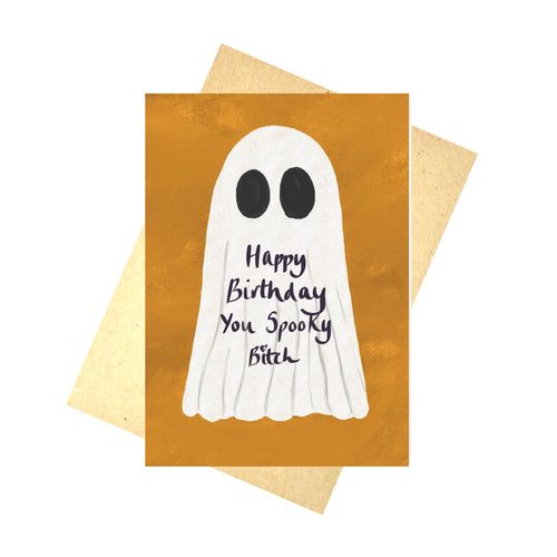 An orange card with a ghost on in sits in front of a recycled brown paper envelope on a white background. The ghost has the words 'Happy Birthday You Spooky Bitch' in purple handwriting below its black eyes.