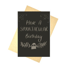 Load image into Gallery viewer, A dark grey card featuring off white handwriting that reads ‘Have A SPOOKTACUALR Birthday’ above a small ghost with leafy vines growing to the sides from behind it. Above the words to the right and left of the card are bat shapes with patterns around them. Behind the card is a brown envelope behind which is a white background.
