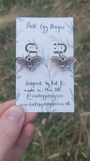 A video of the hoops earrings with bat charms. The earrings are hanging from a white backing card with a black leafy vine design and the words 'Duck Egg Designs' handwritten across the top.