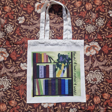 Load image into Gallery viewer, A white tote lies on a brown retro floral patterned background. The bag features a book shelf with colourful books and a trailing philodendron in front of a green textured background. To the right of the bookcase are the words ‘Hoarder of books, explorer of worlds’ in black handwriting running down the side. Across the spine of one of the books is the black Duck Egg Designs logo.
