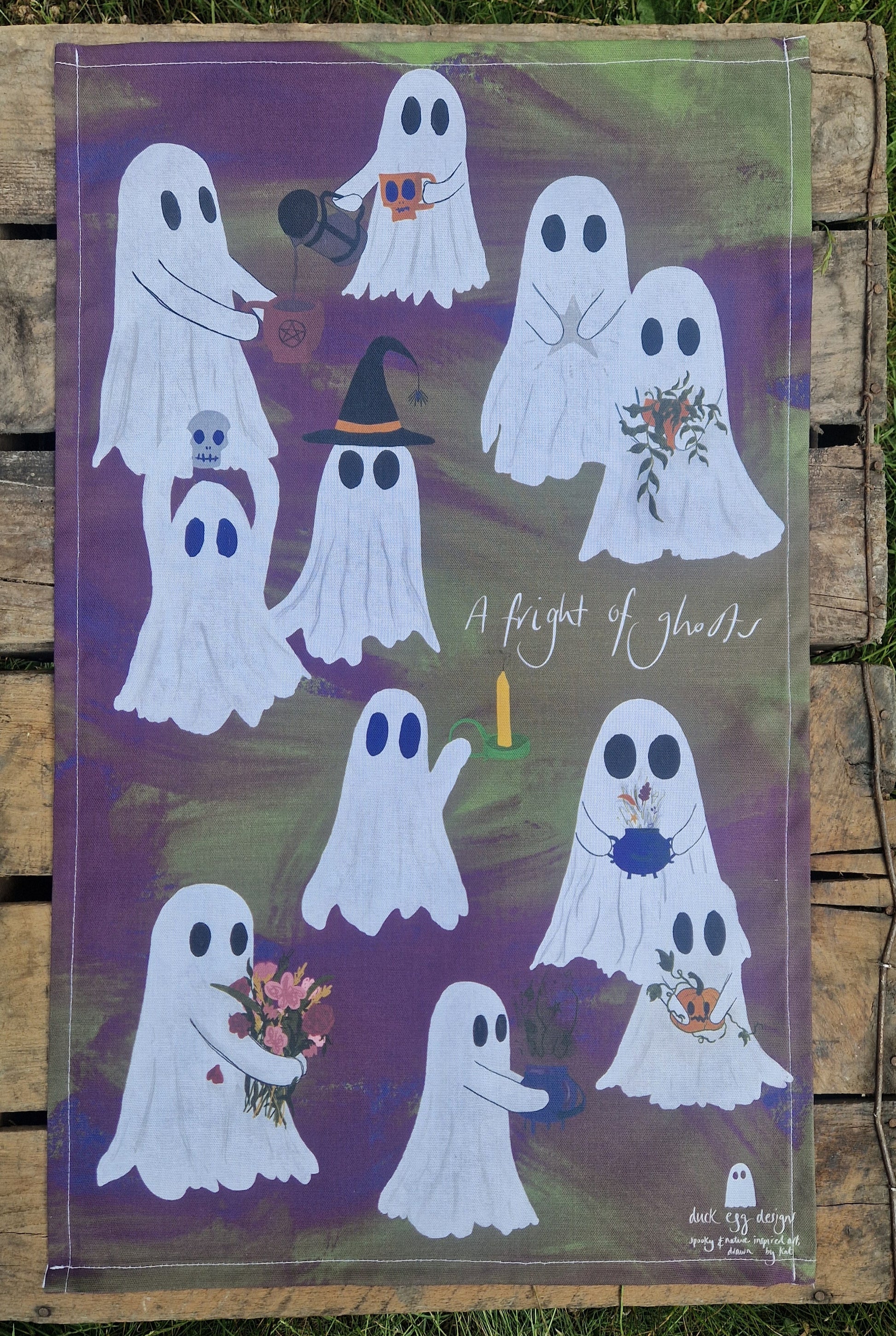 Decorative tea towel with ghost illustrations on a wooden surface