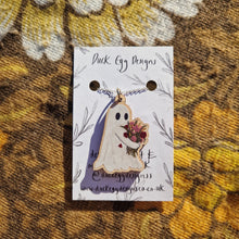 Load image into Gallery viewer, A white ghost holding a bunch of red, pink and dusky yellow flowers sits on a silver necklace chain. The necklace is attached to a white backing card with the words ‘ Duck Egg Designs’ in black handwriting as well as a leafy vine design. In the background you can see a retro floral patterned warm brown fabric.
