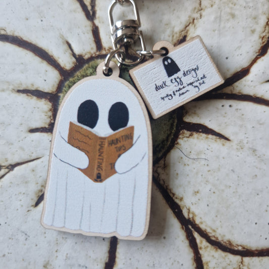The Reading Ghost Keyring by Duck Egg Designs features a cartoon ghost reading "Haunting Tips" and includes a smaller tag with a ghost drawing and handwritten text on a marbled background.