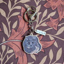 Load image into Gallery viewer, A grey and tortoiseshell cat keyring sits on a retro brown floral patterned background. He keyring has silver hardware and a small charm with the duck egg designs logo.
