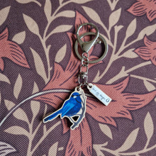 Load image into Gallery viewer, A blue fairy wren keyring sits on a brown retro floral background. The keyring has a second white smaller charm with the duck egg designs logo.

