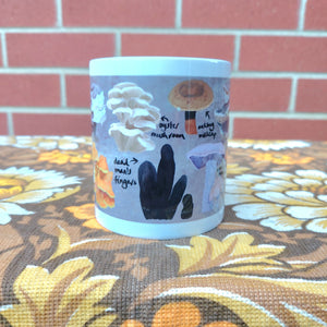 The middle section of a white mug with a fungi design on it. Under the mug is a warm brown retro floral fabric in front of a red brick wall.